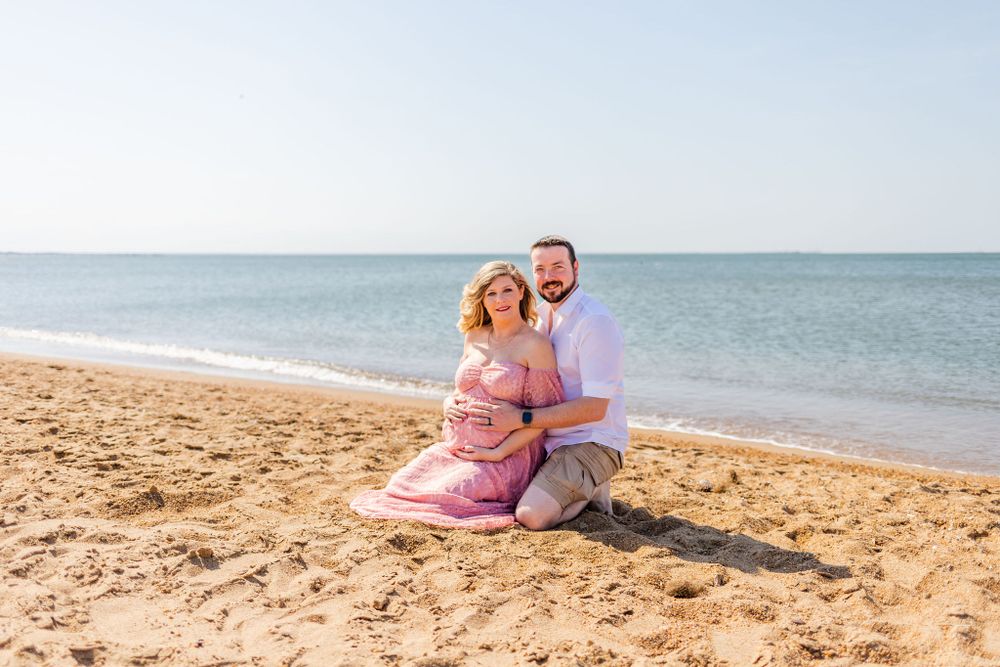 Couple embracing on sandy beach during maternity photo session.