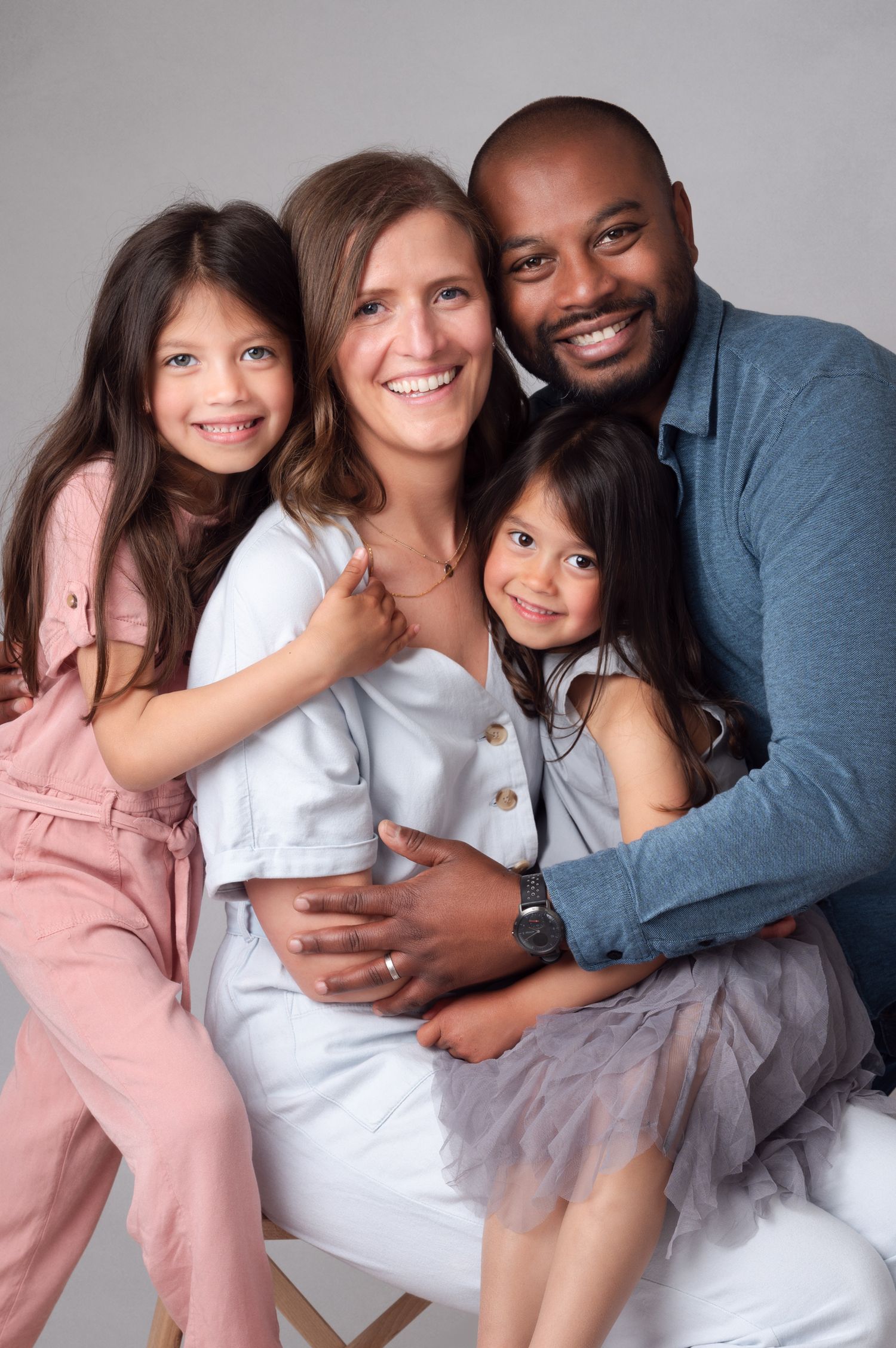 Modern diverse family portrait with parents and two young daughters in coordinated neutral outfits.