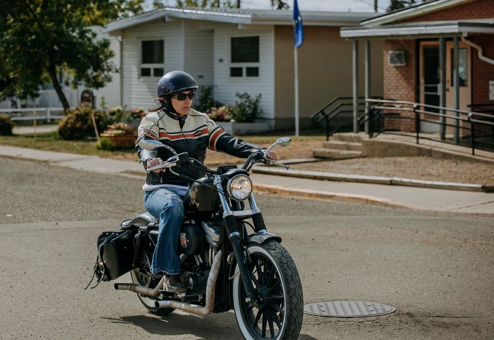 Motorcyclist riding a custom cruiser bike along a residential driveway.