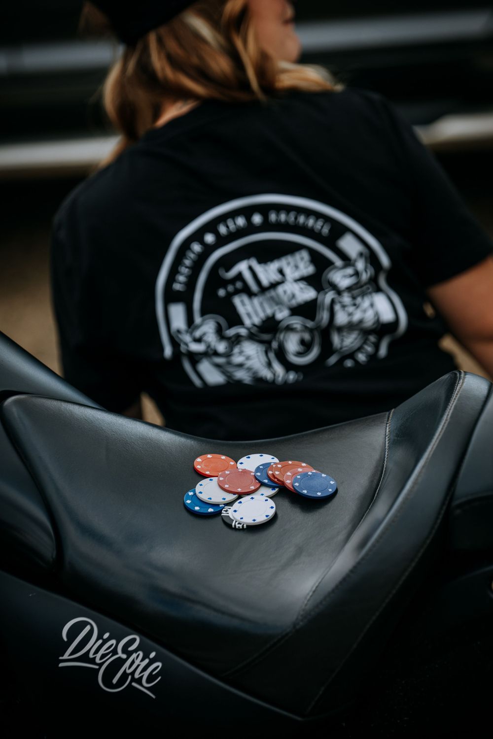 Red white and blue poker chips displayed on leather motorcycle seat with black shirt logo.