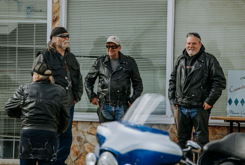 Group of bikers gathered around blue motorcycle during outdoor event.