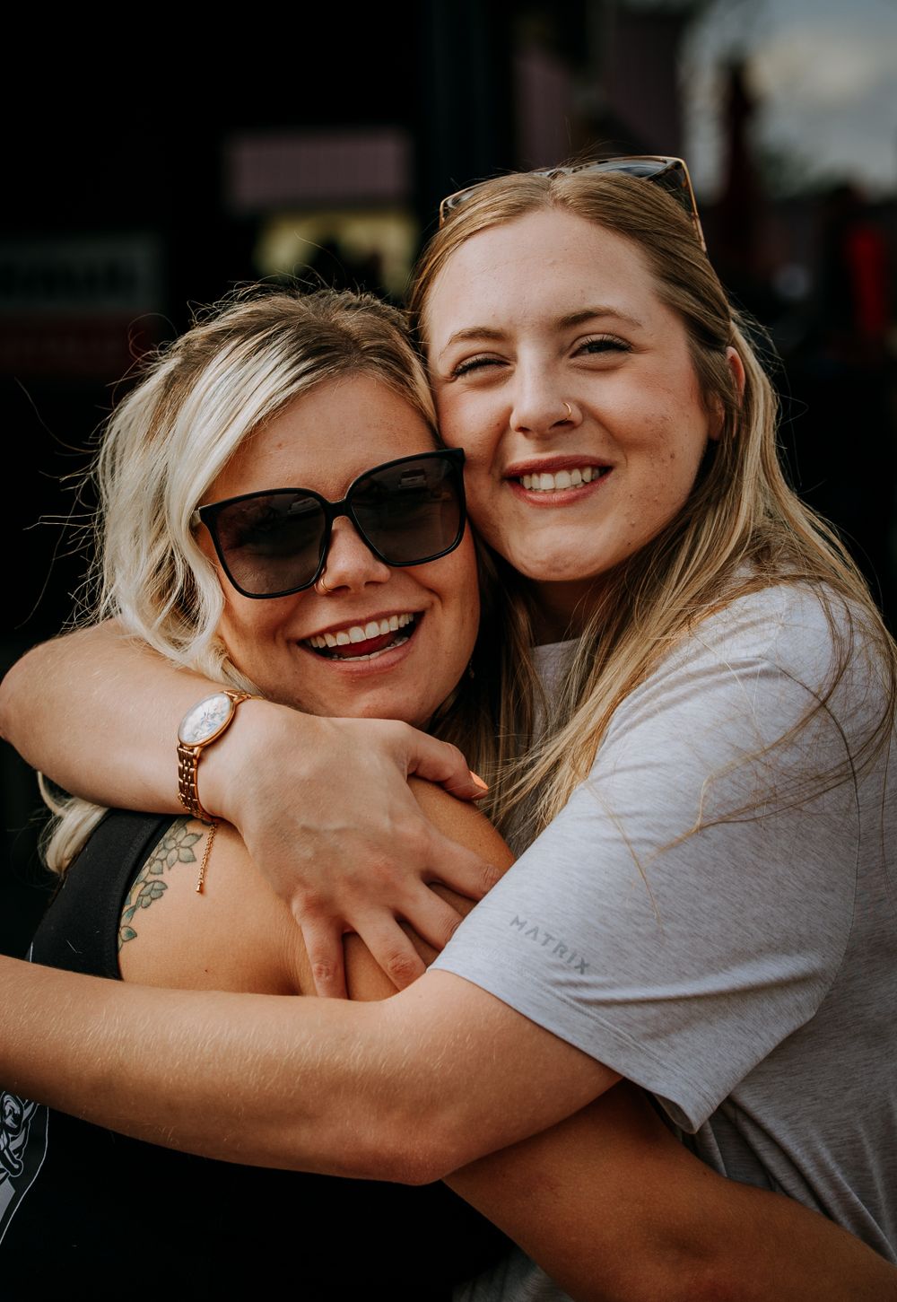 Two friends sharing a warm embrace and laughing together outdoors on a sunny day.