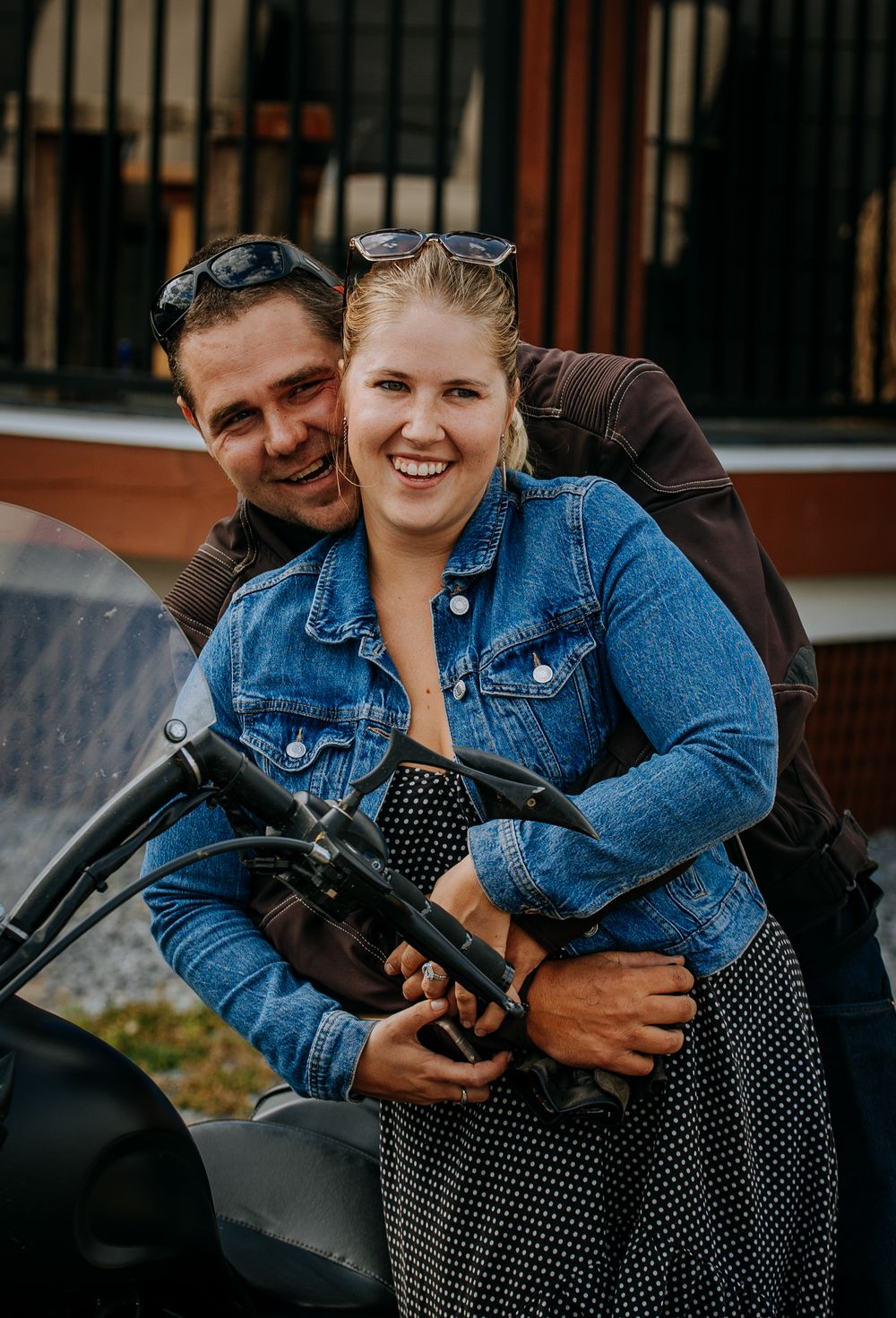 Couple posing on a motorcycle together, wearing casual denim and leather.