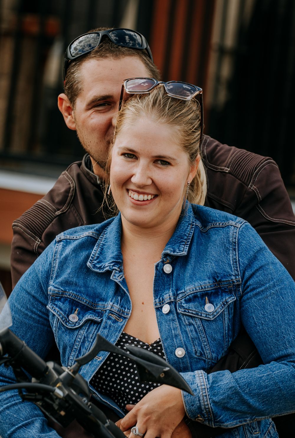Close-up shot of a couple smiling while seated on a motorcycle together.