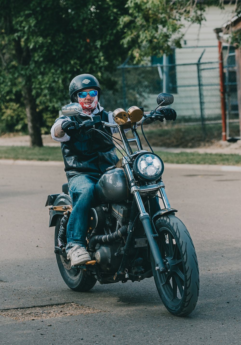 Motorcyclist in dark gear riding a black cruiser bike on a residential street.