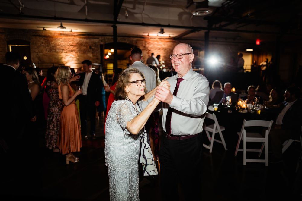 Dance floor moment at wedding reception in rustic industrial venue with mood lighting.
