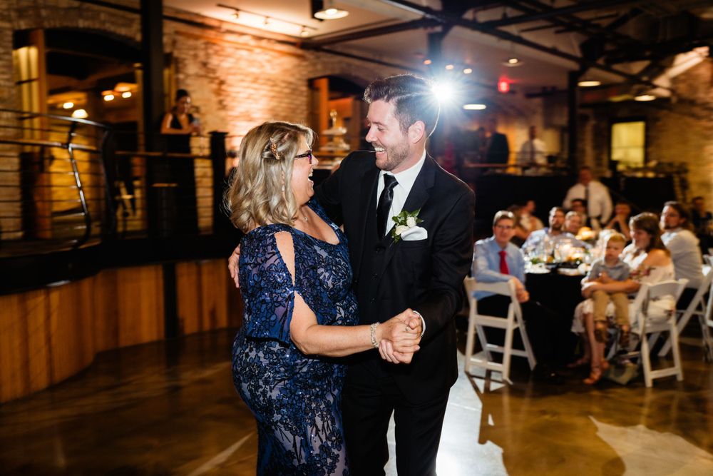 Wedding reception dance in an industrial-style venue with brick walls and mood lighting.