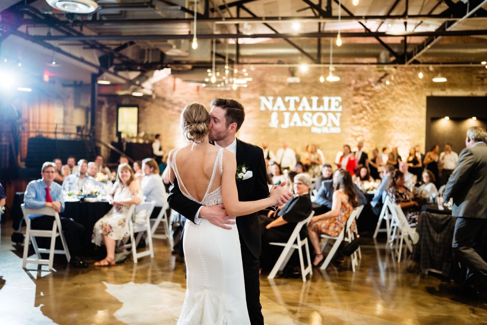 Wedding reception first dance in an industrial venue with illuminated name sign.