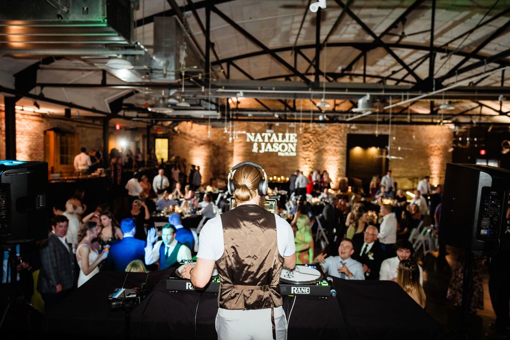 Wide shot of crowded wedding reception dance floor with illuminated venue name sign.