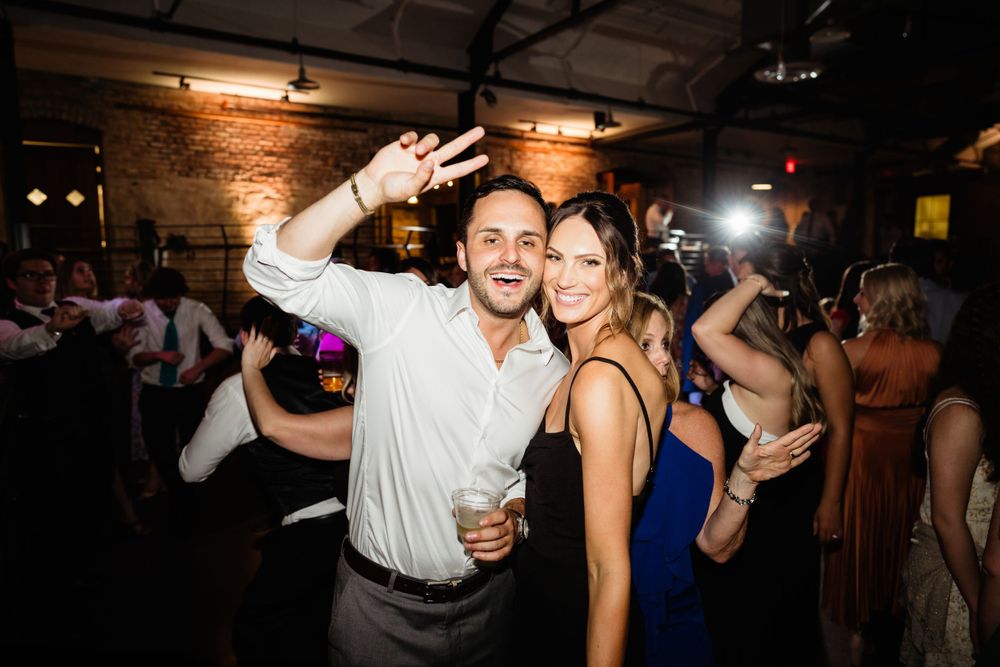 Wedding reception party scene with guests dancing under ambient lighting.