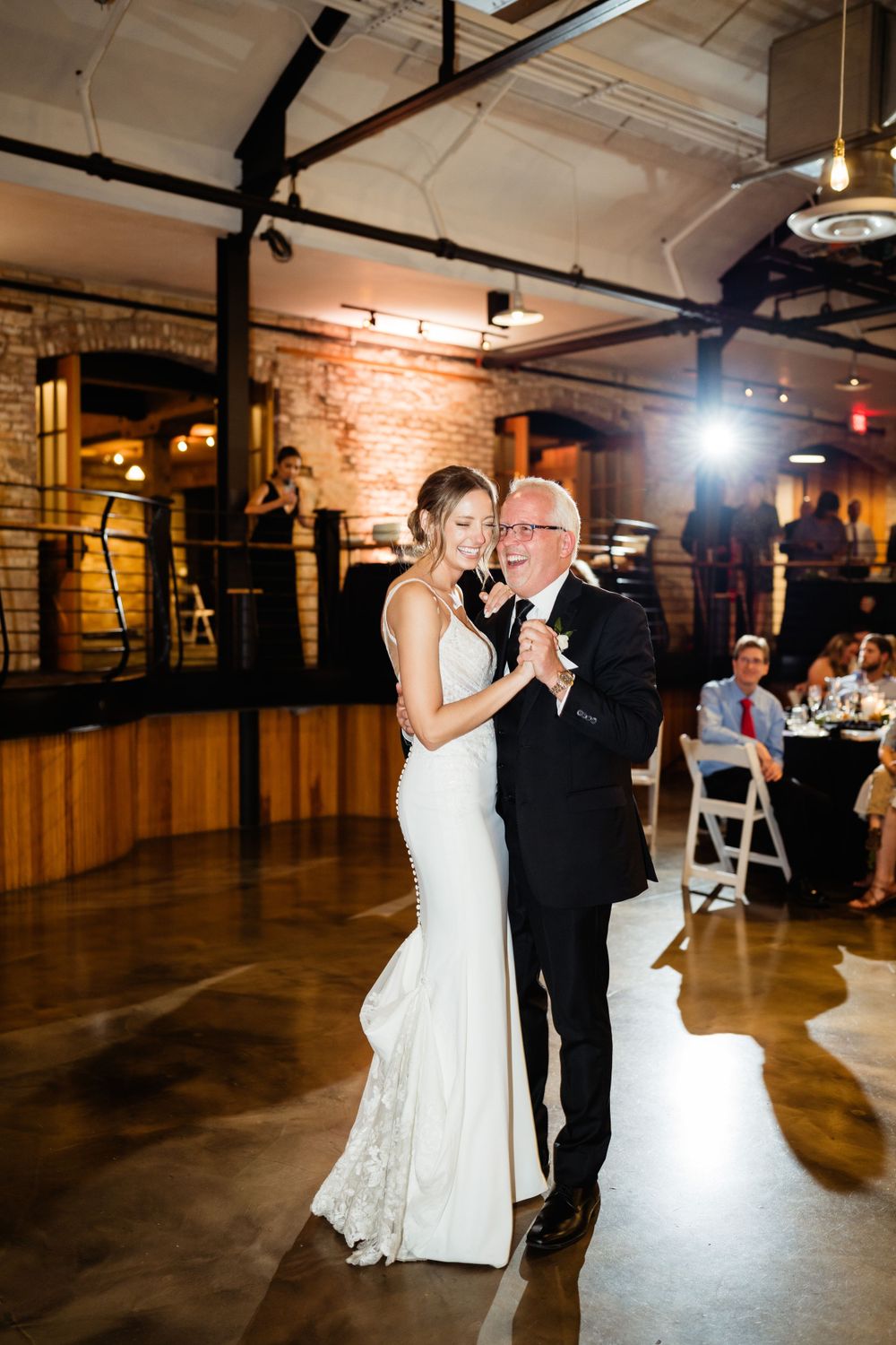 Elegant wedding dance in a rustic venue with exposed brick walls and ambient lighting.