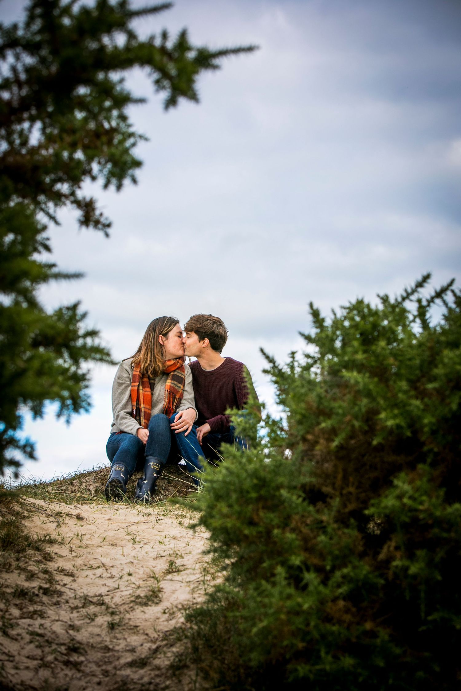 Romantic couple sitting together on a sandy hill surrounded by evergreen trees.