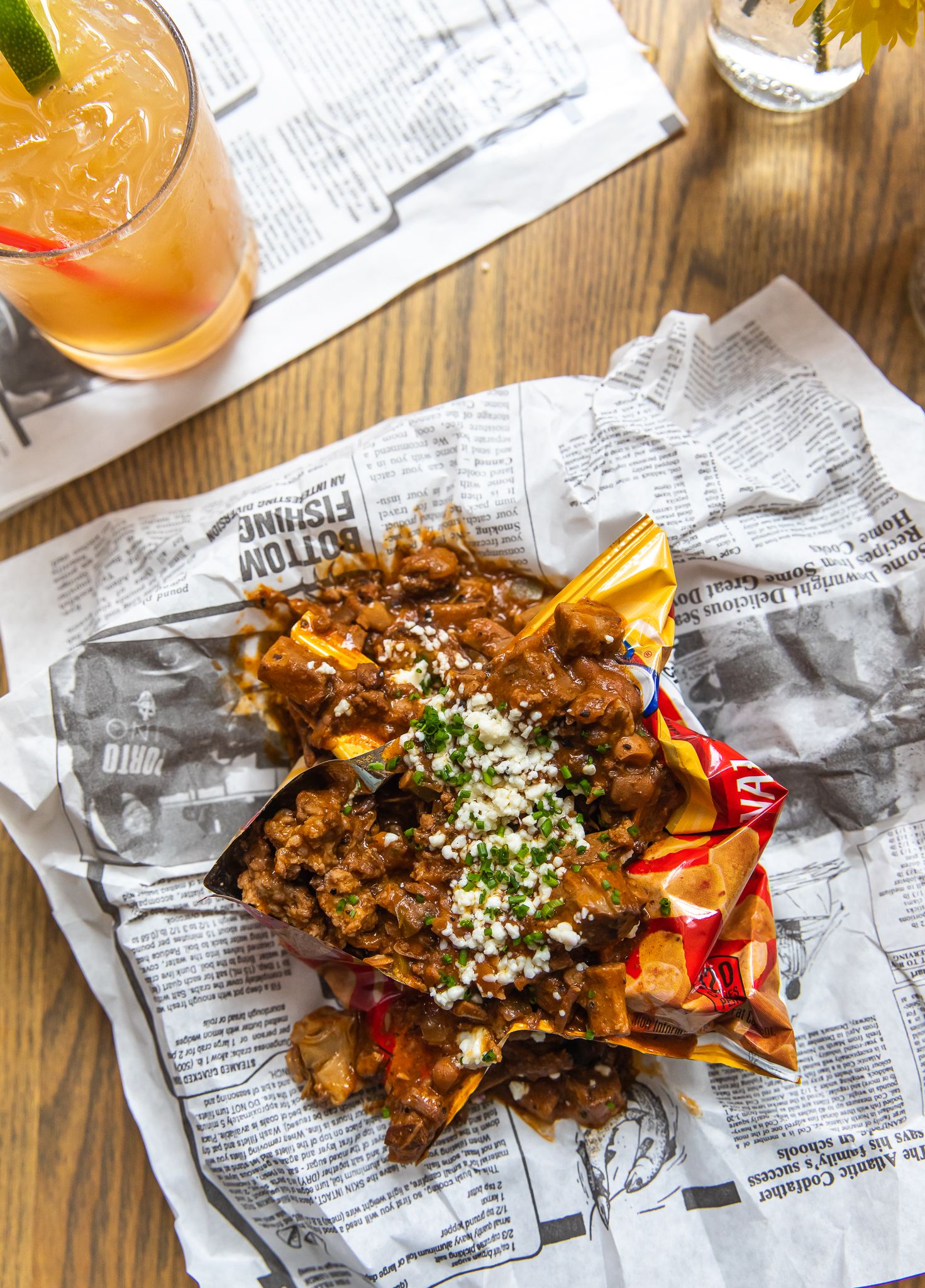 Loaded street fries topped with cheese and herbs served on newspaper with cocktail.