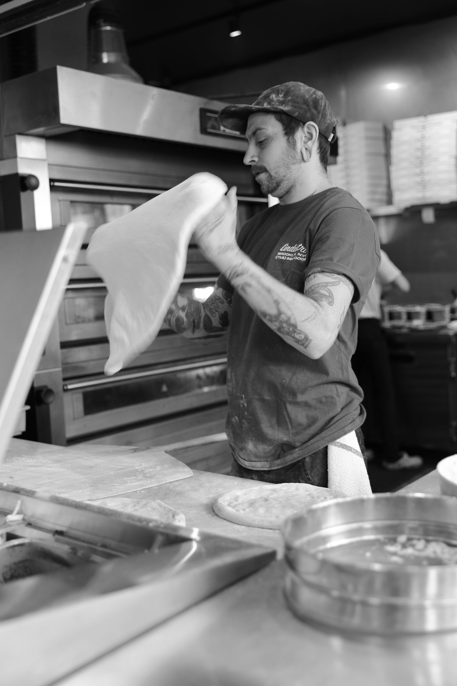 Restaurant worker tossing and shaping pizza dough at a prep station.