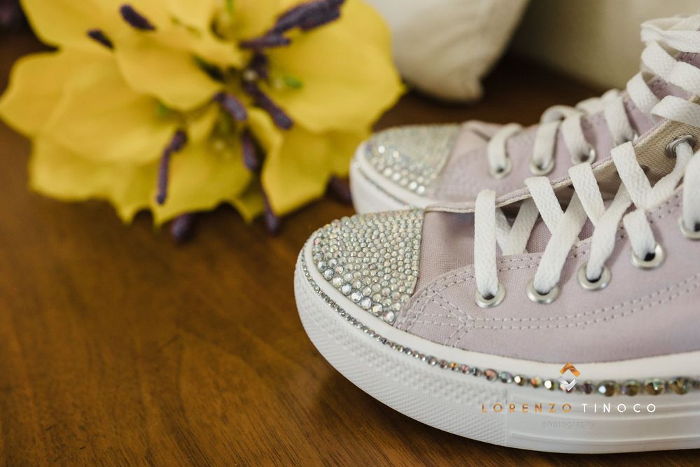 Pink sparkly sneaker with rhinestone details next to yellow flower on wooden surface.
