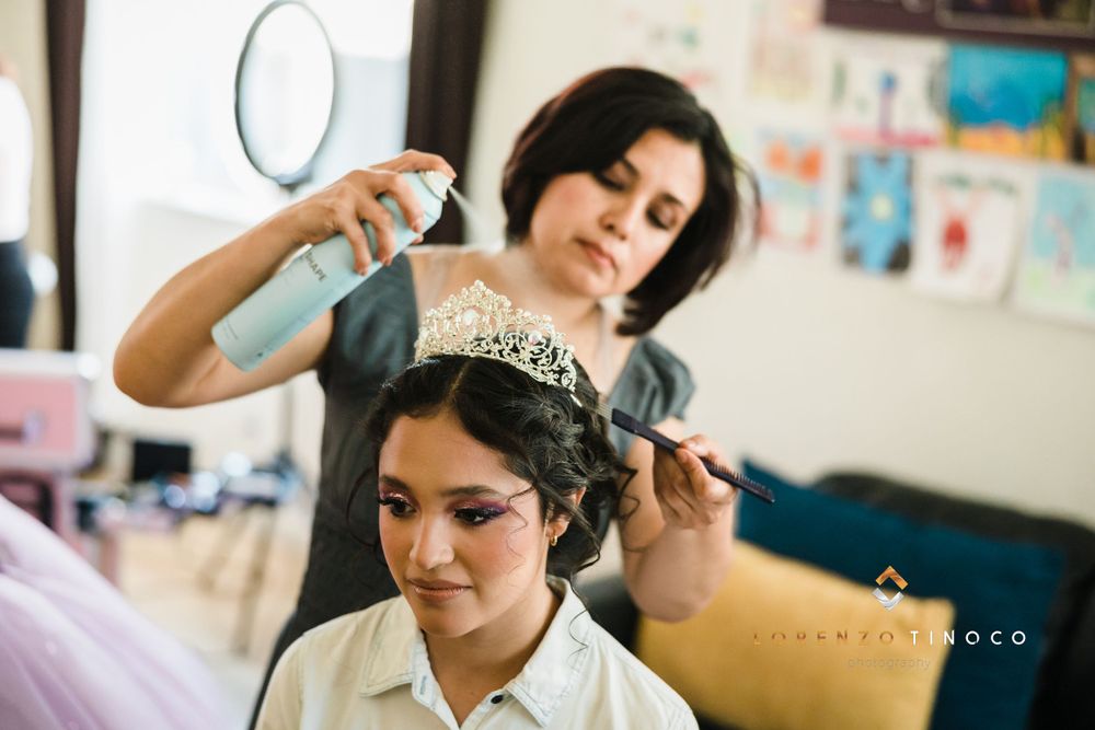 Hairstylist applying hairspray while adjusting an ornate tiara during preparation.