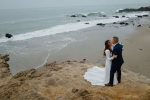 Sioux City, Iowa photographer. Bride and groom stand on rocky cliffside overlooking ocean waves on their beach wedding day.