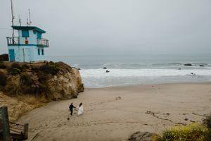 Sioux City, Iowa photographer. Bride and groom walking on sandy beach near blue lifeguard tower on overcast day.