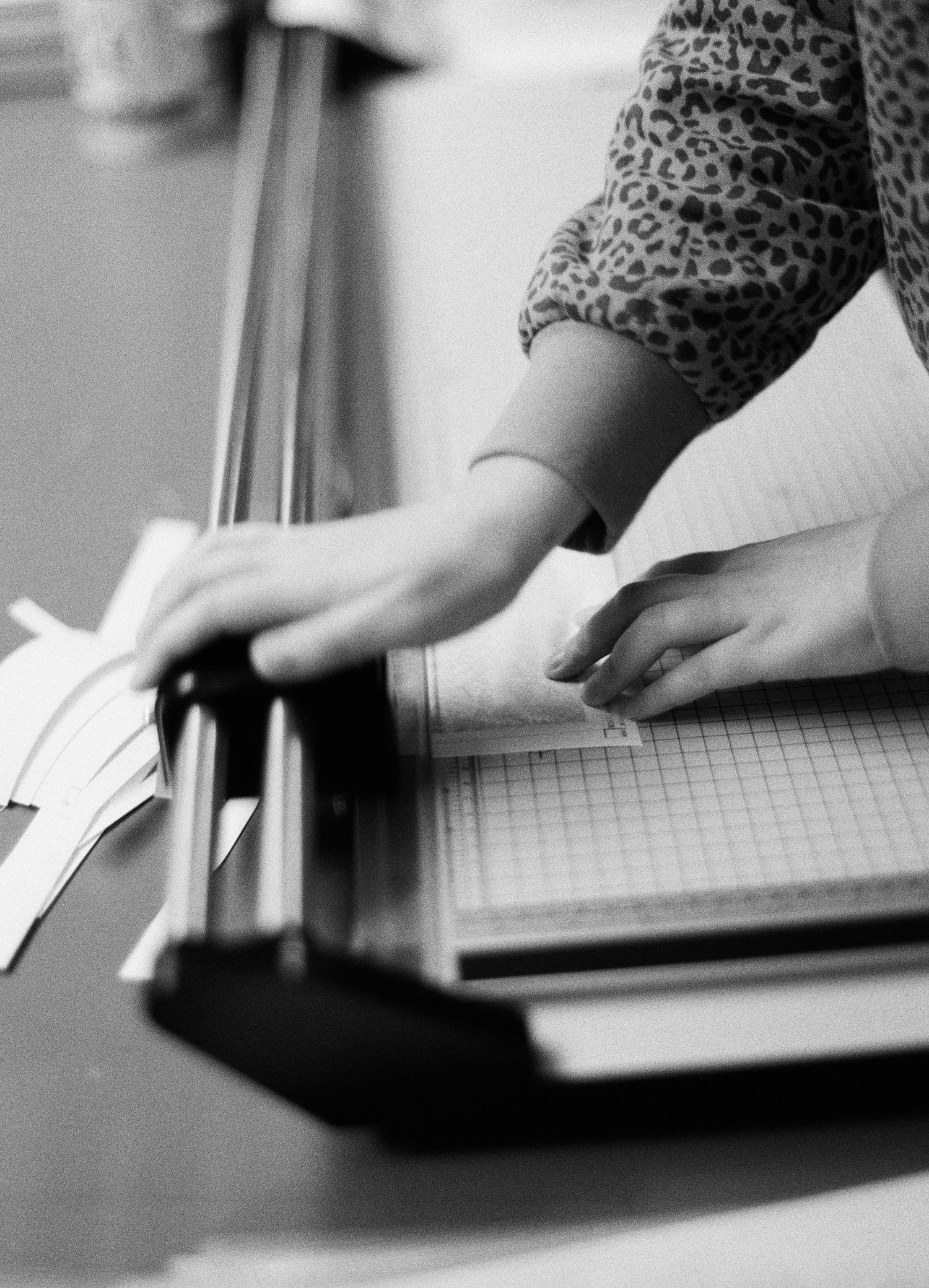Hands working with a paper trimmer or cutting board in black and white.
