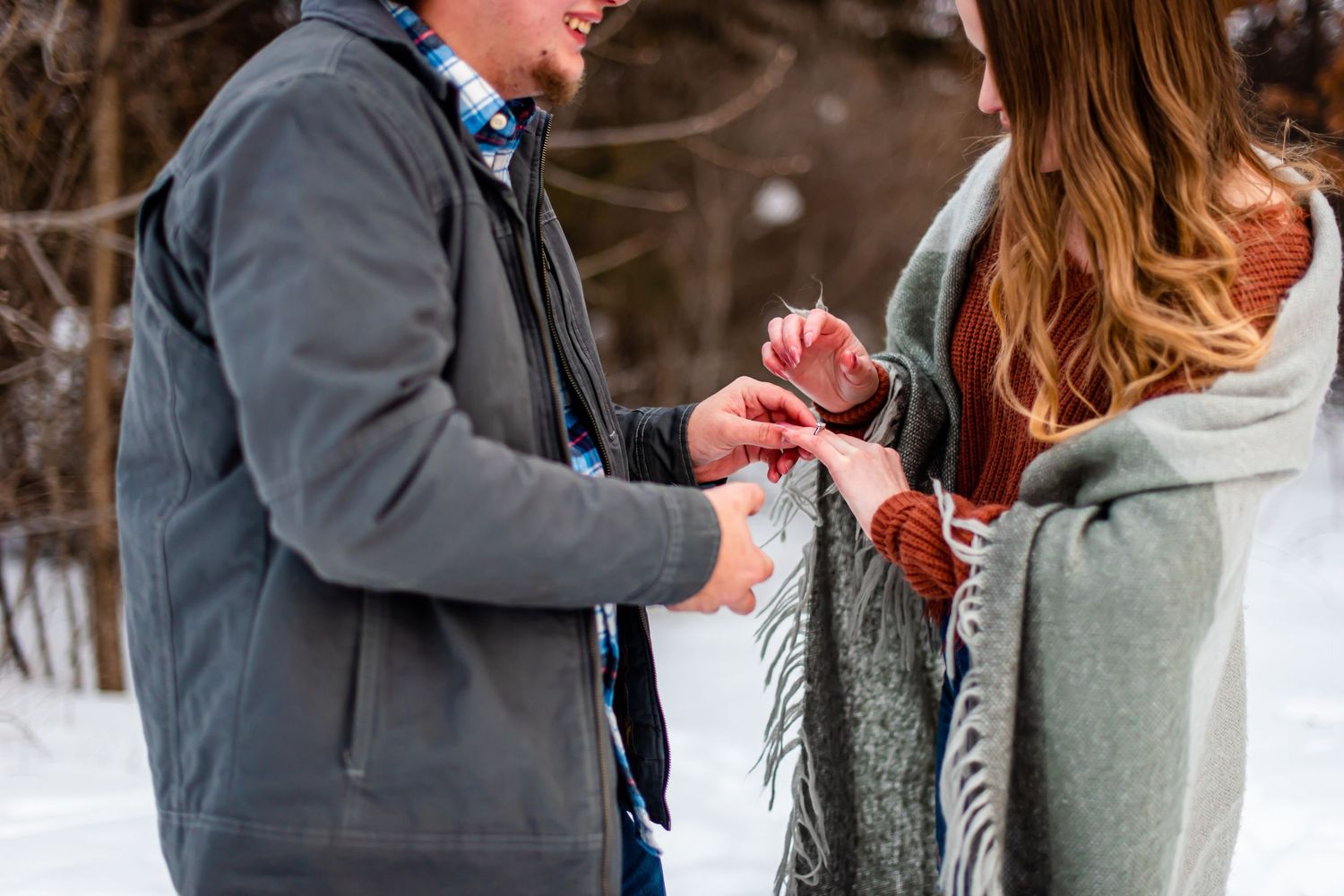 Close-up shot of hands exchanging a ring during a winter engagement outdoors.