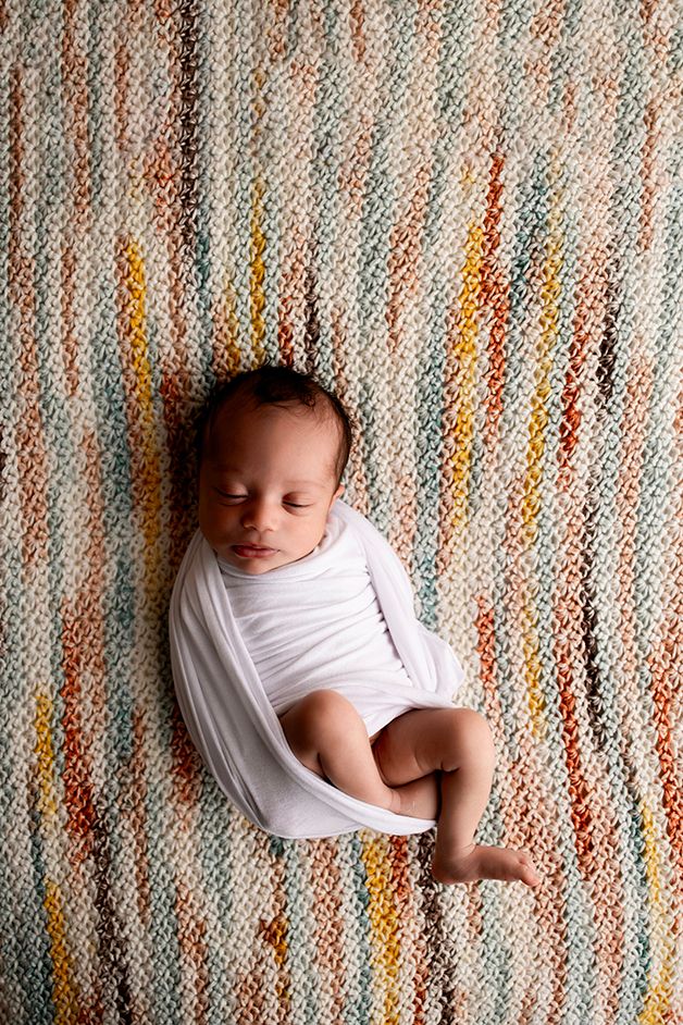 Newborn girl on heirloom crocheted blanket wrapped in a white wrap.
