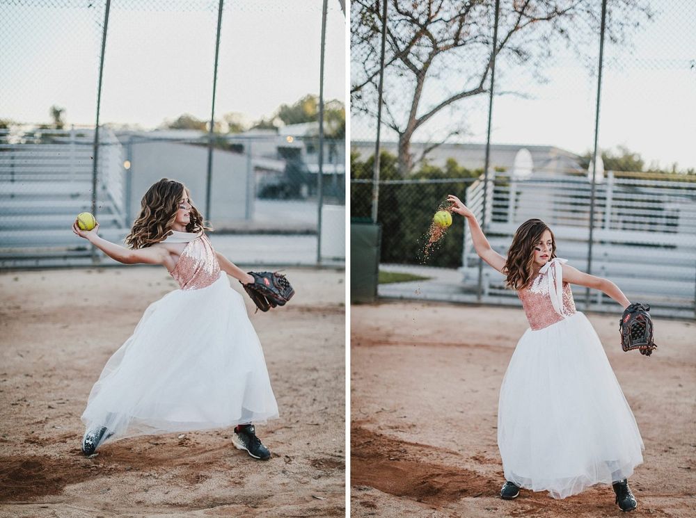 A bride in a flowing white dress takes a playful swing at a baseball on a dirt field at sunset.