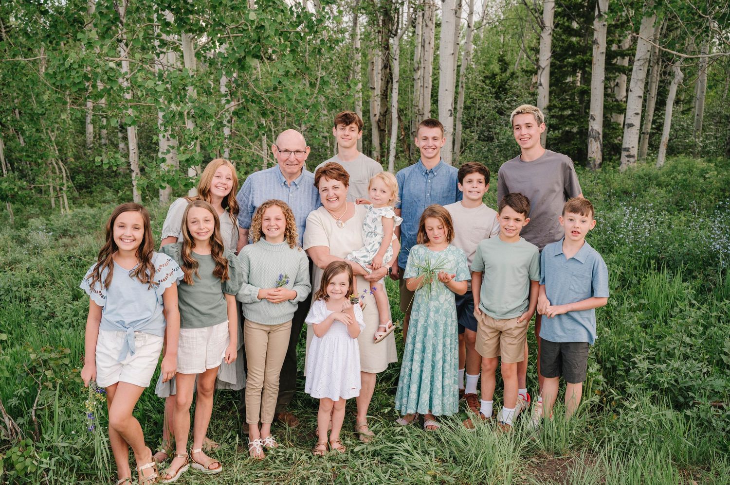 Group photo of people in coordinated casual clothing standing together in aspen forest setting.