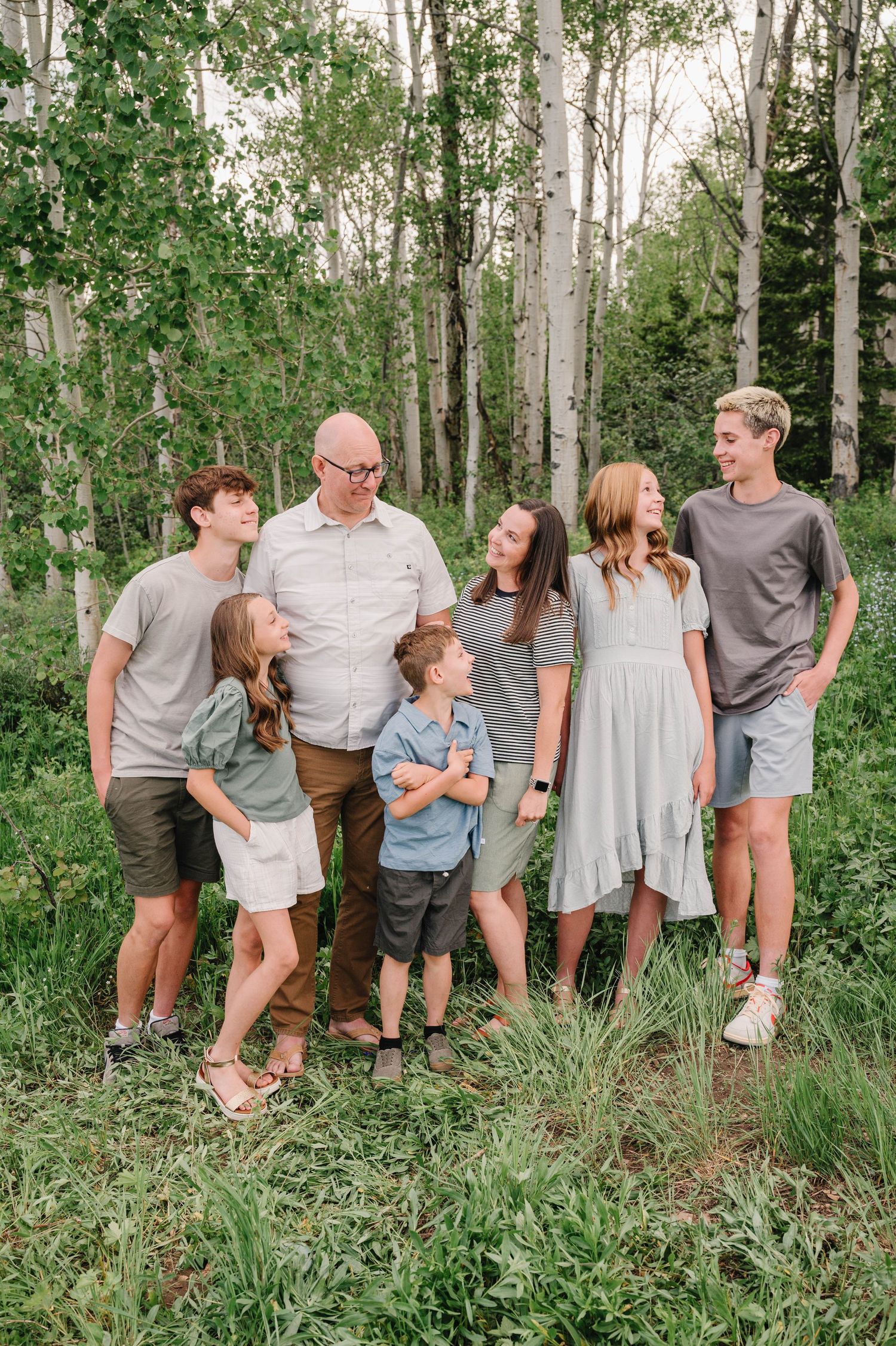 Family group laughing together during outdoor portrait session in wooded mountain setting.