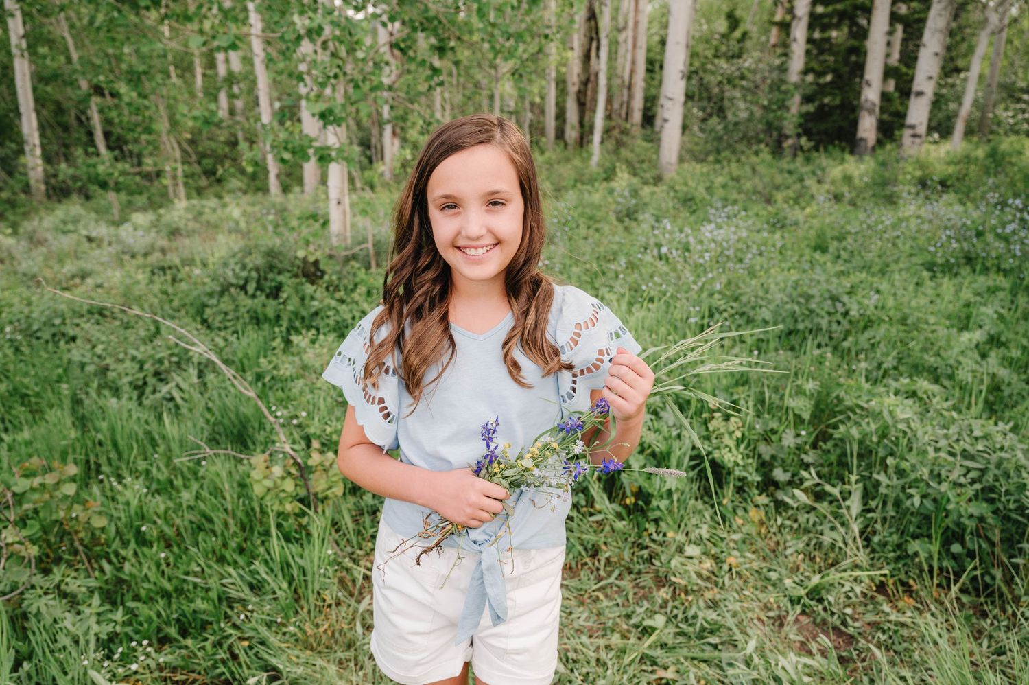 Young person in light blue top poses against background of aspen trees in mountain setting.