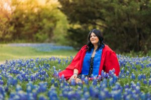 high school senior girl smiling in red graduation gown in bluebonnet flowers