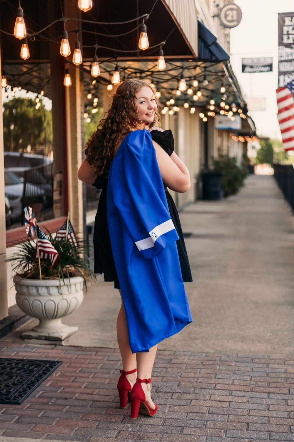 high school senior girl with curly hair smiling holding her graduation gown in downtown midlothian Texas