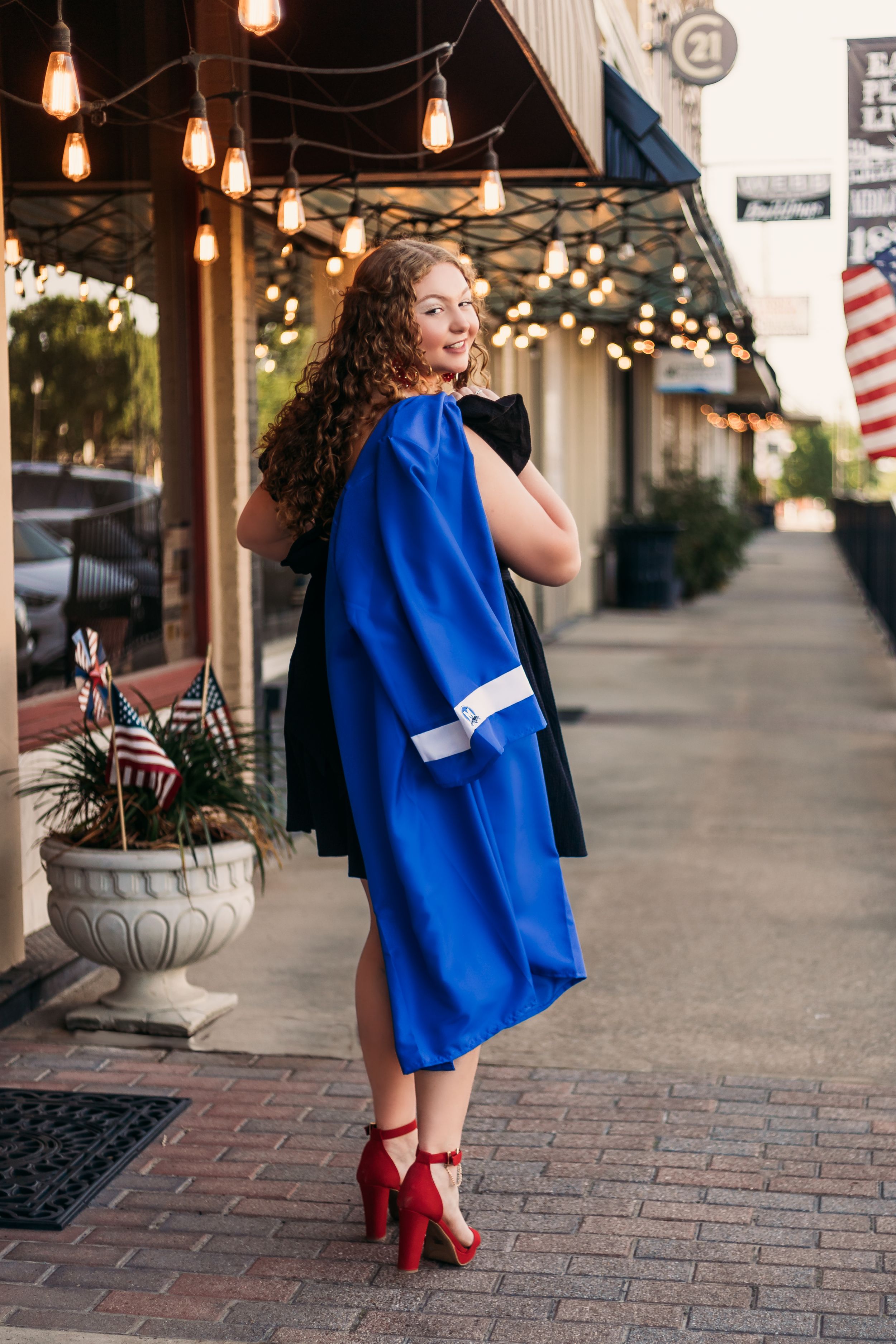 high school senior girl with curly hair smiling holding her graduation gown in downtown midlothian Texas