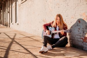 high school senior girl playing guitar in sunlight in downtown midlothian Texas Dallas
