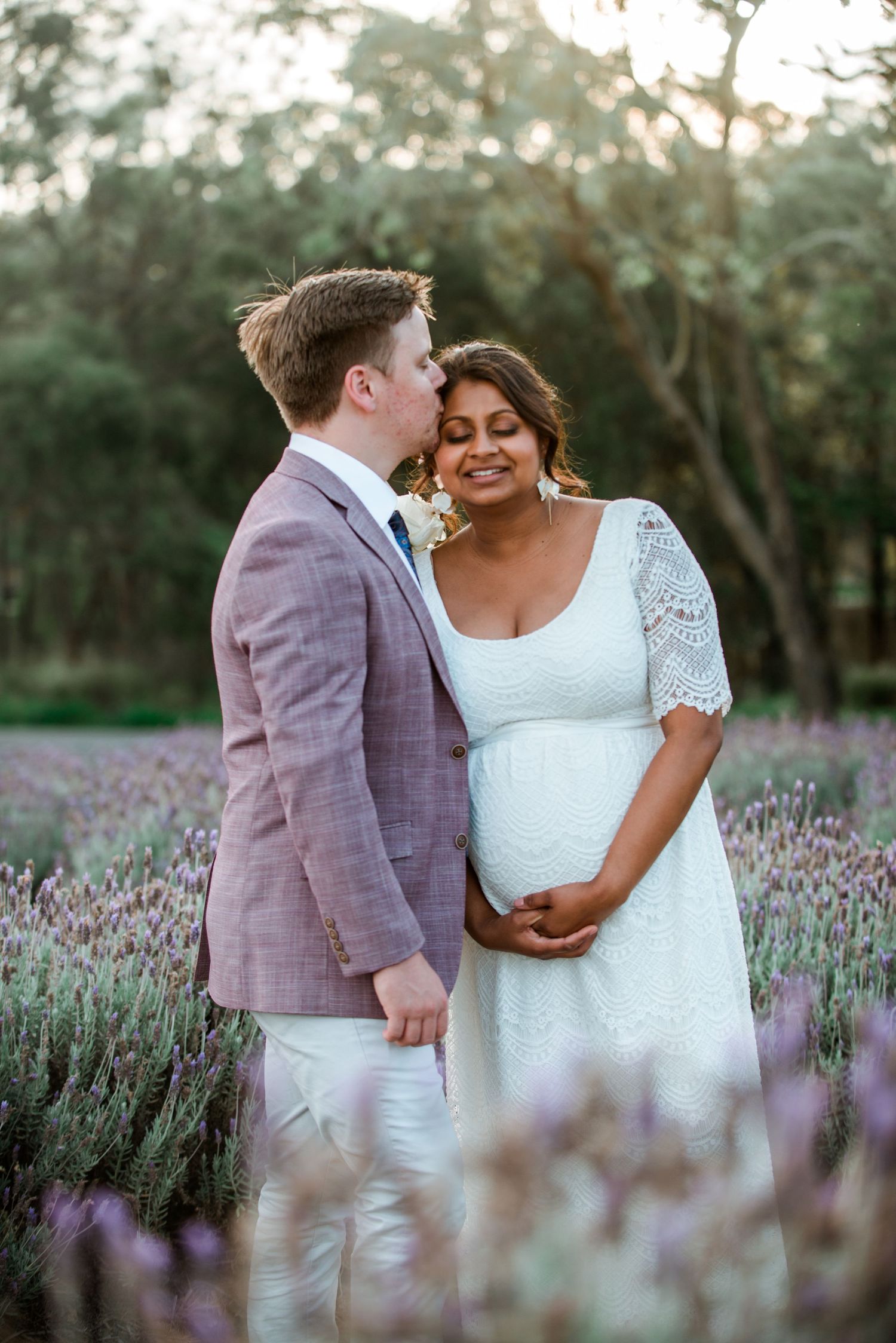 A couple embraces in a lavender field while wearing wedding attire.
