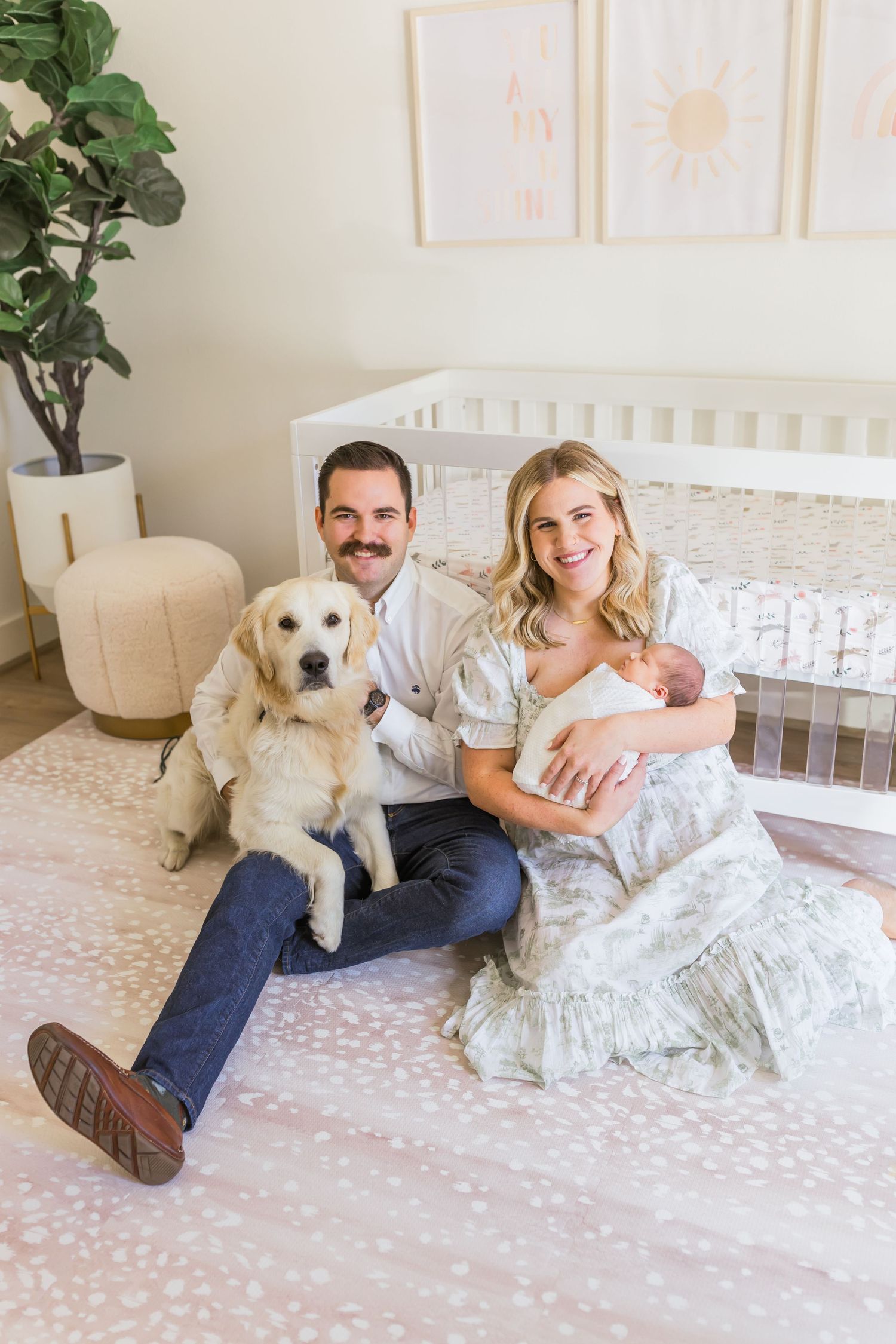 Family portrait in nursery with golden retriever and newborn by white crib.