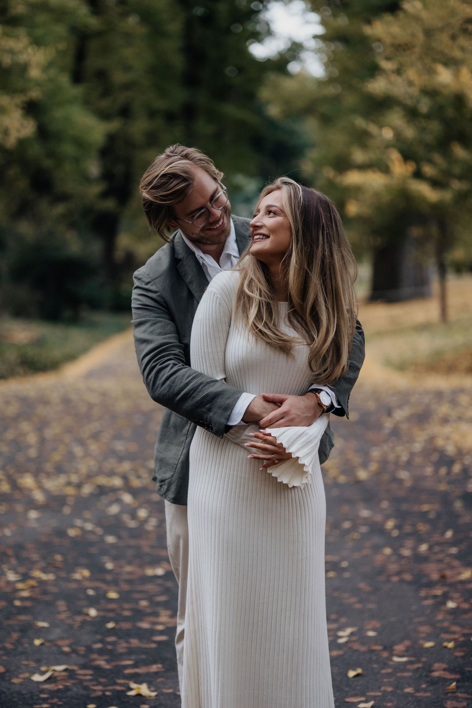 Intimate embrace between couple in autumn park setting with fallen leaves.