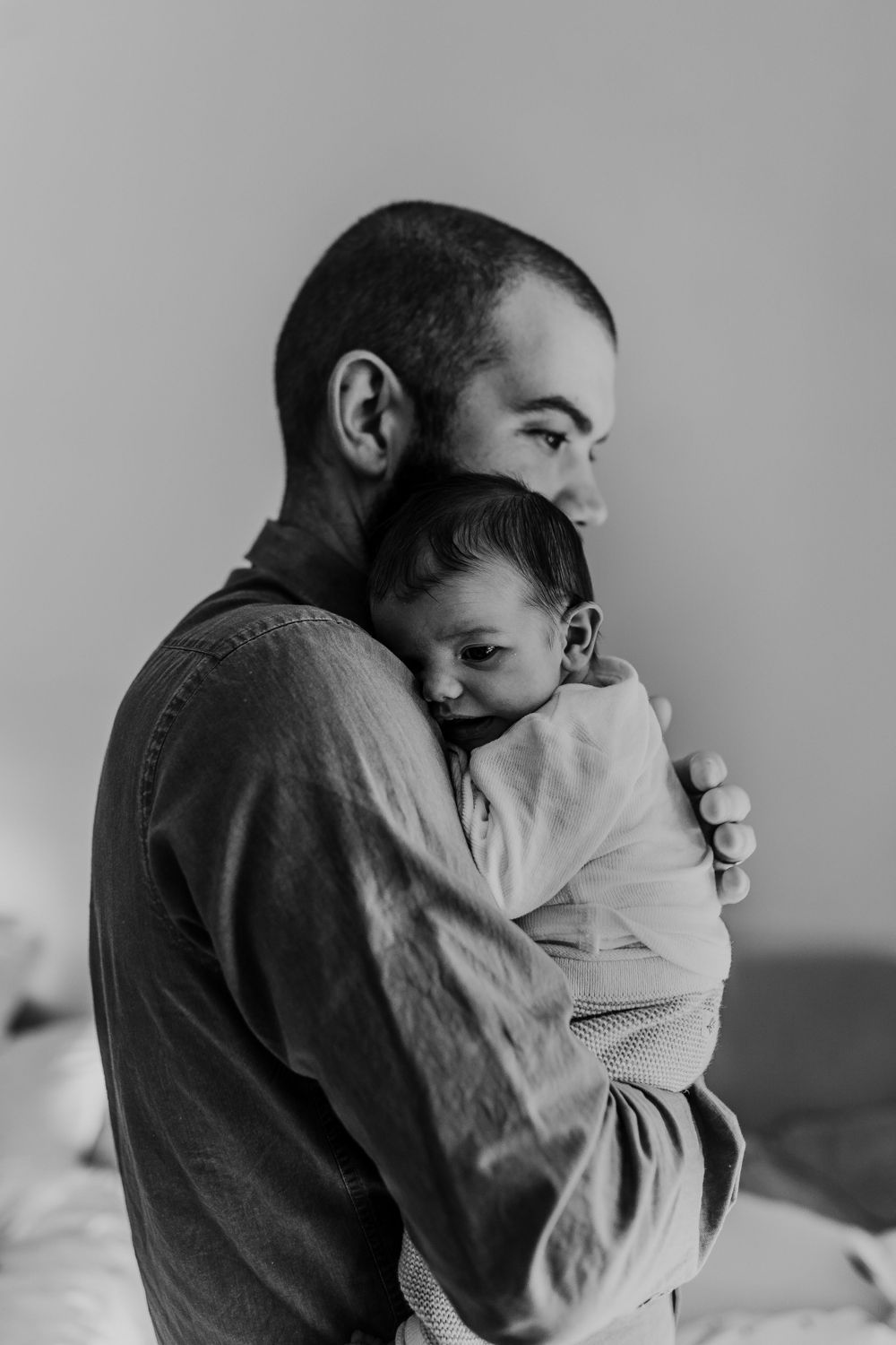 Black and white portrait of bearded parent cradling sleeping infant against shoulder.