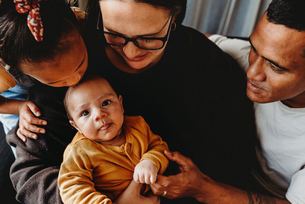 Family enjoying tender moment with baby in mustard yellow sweater as they gather close together on couch.