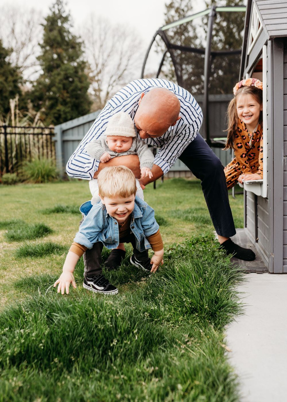 A playful outdoor family scene shows adults and children laughing together by a house.