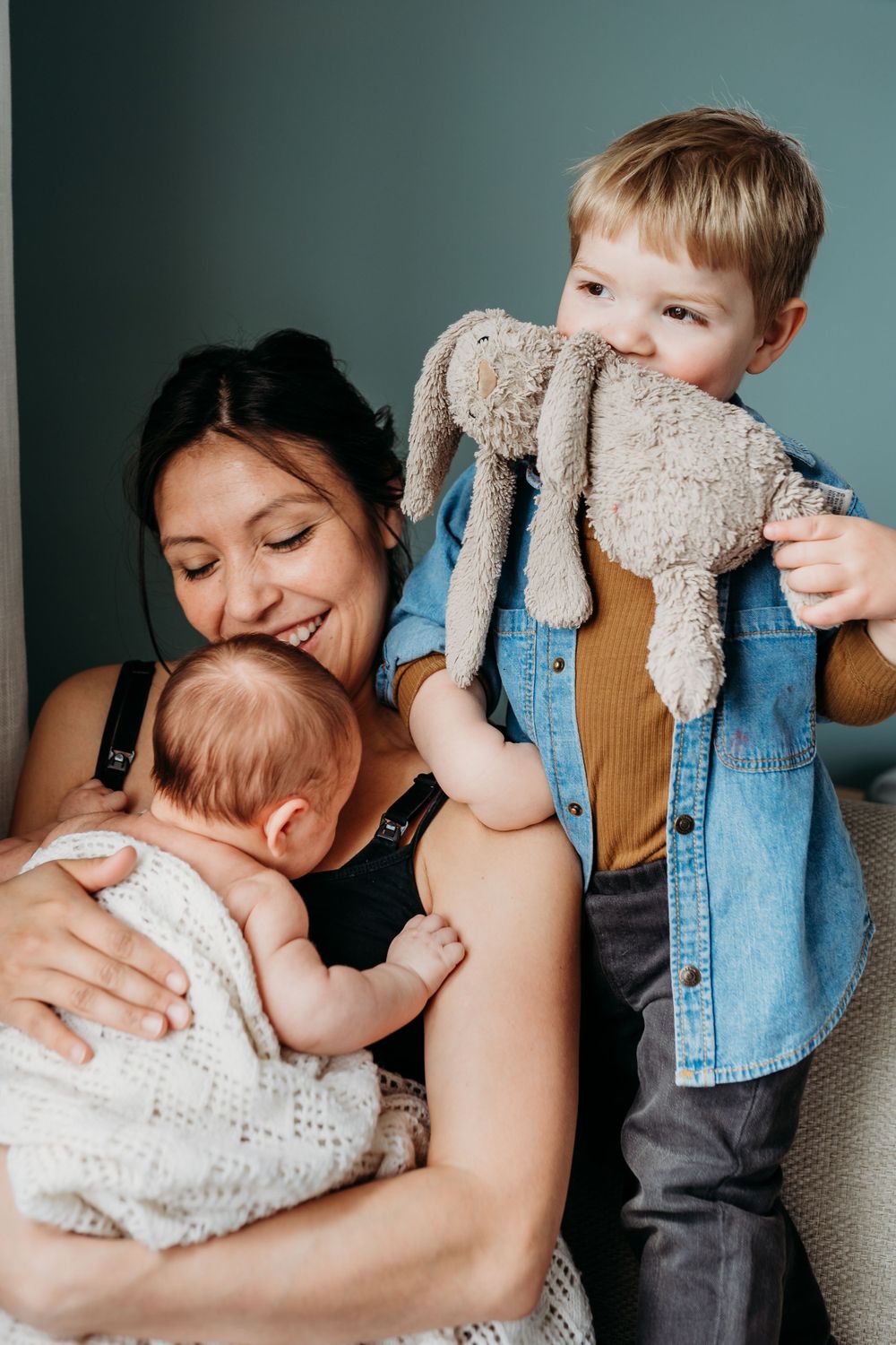 A heartwarming family moment shows a parent holding a baby while another child hugs their stuffed animal.