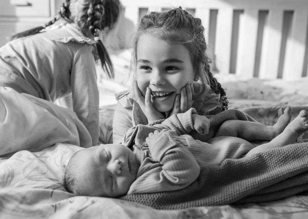 A heartwarming moment with a newborn baby being admired on a bed.