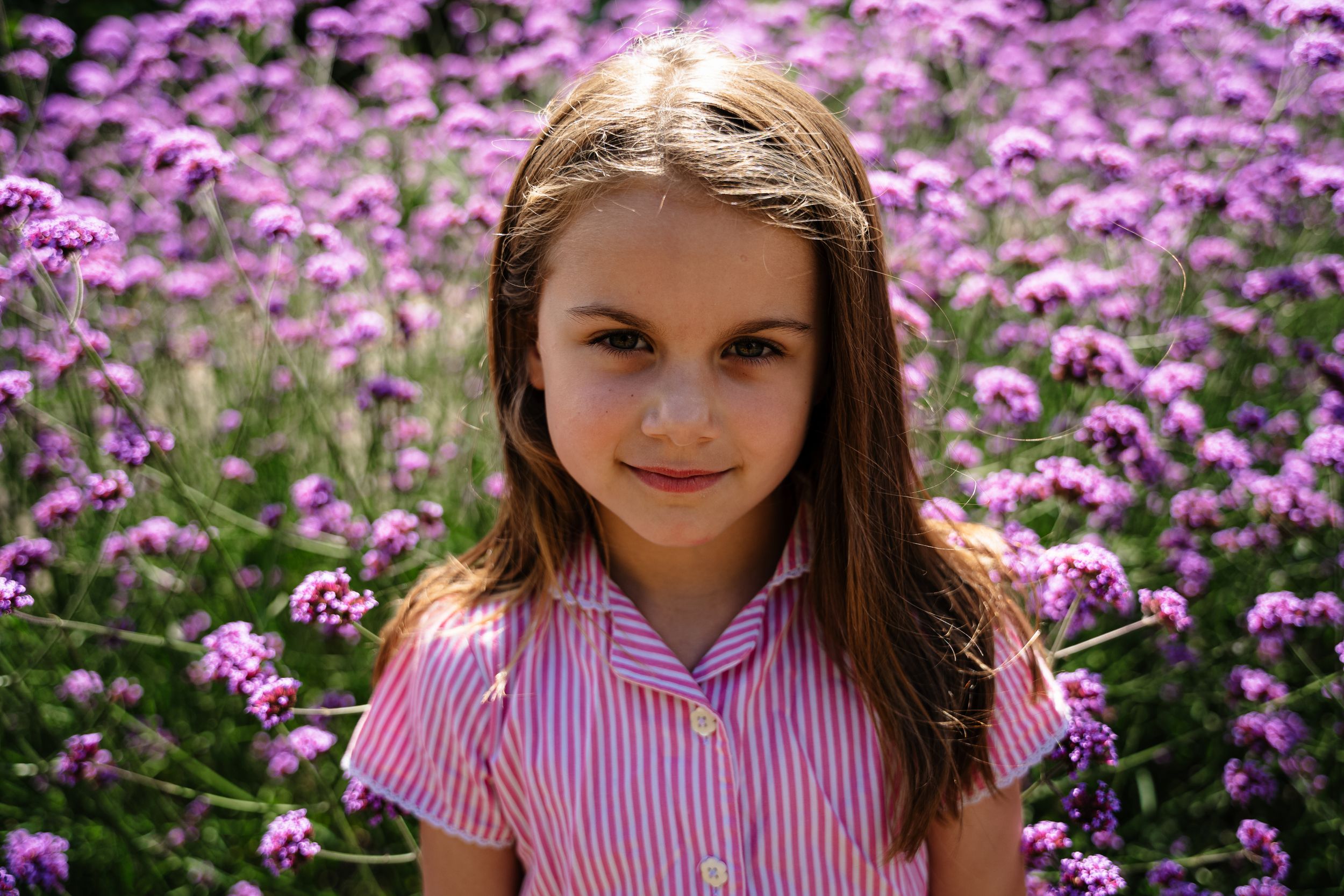A portrait among purple wildflowers wearing a pink striped dress.