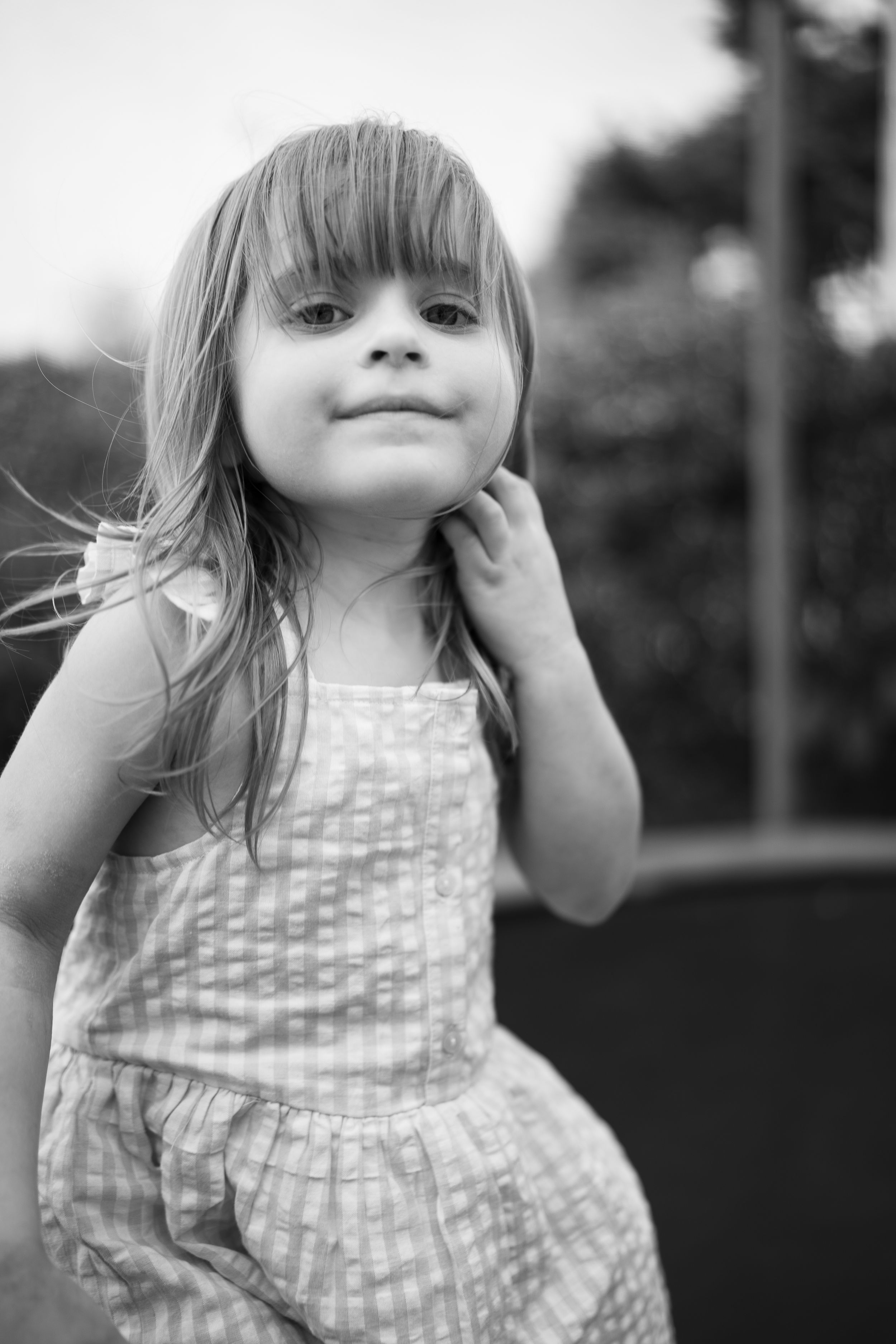 Black and white portrait of a child in patterned dress touching their neck with gentle expression.