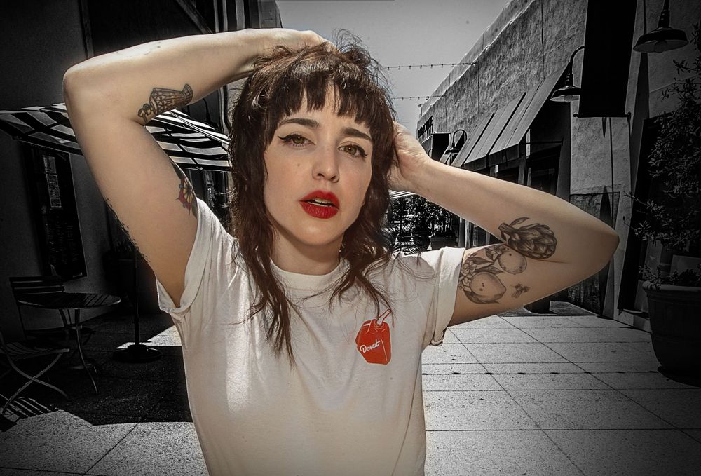 Black and white portrait of a woman in a white t-shirt with tattoos and red lipstick.