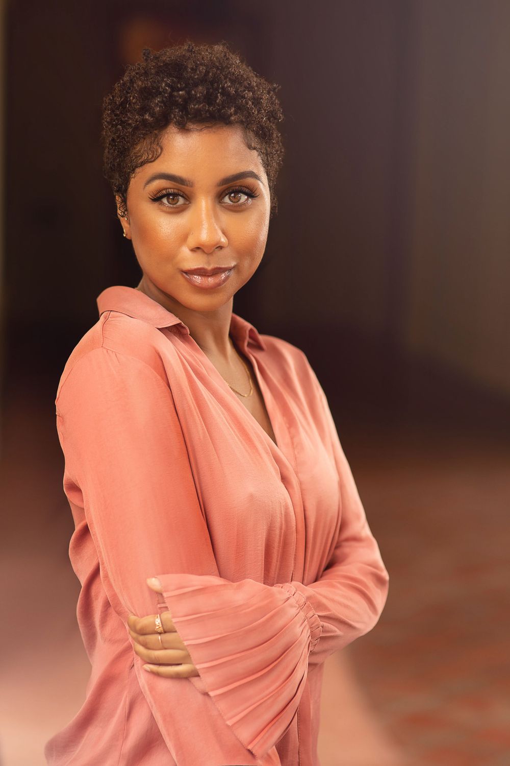 Professional portrait of a woman in a flowing coral blouse against a warm-toned background.