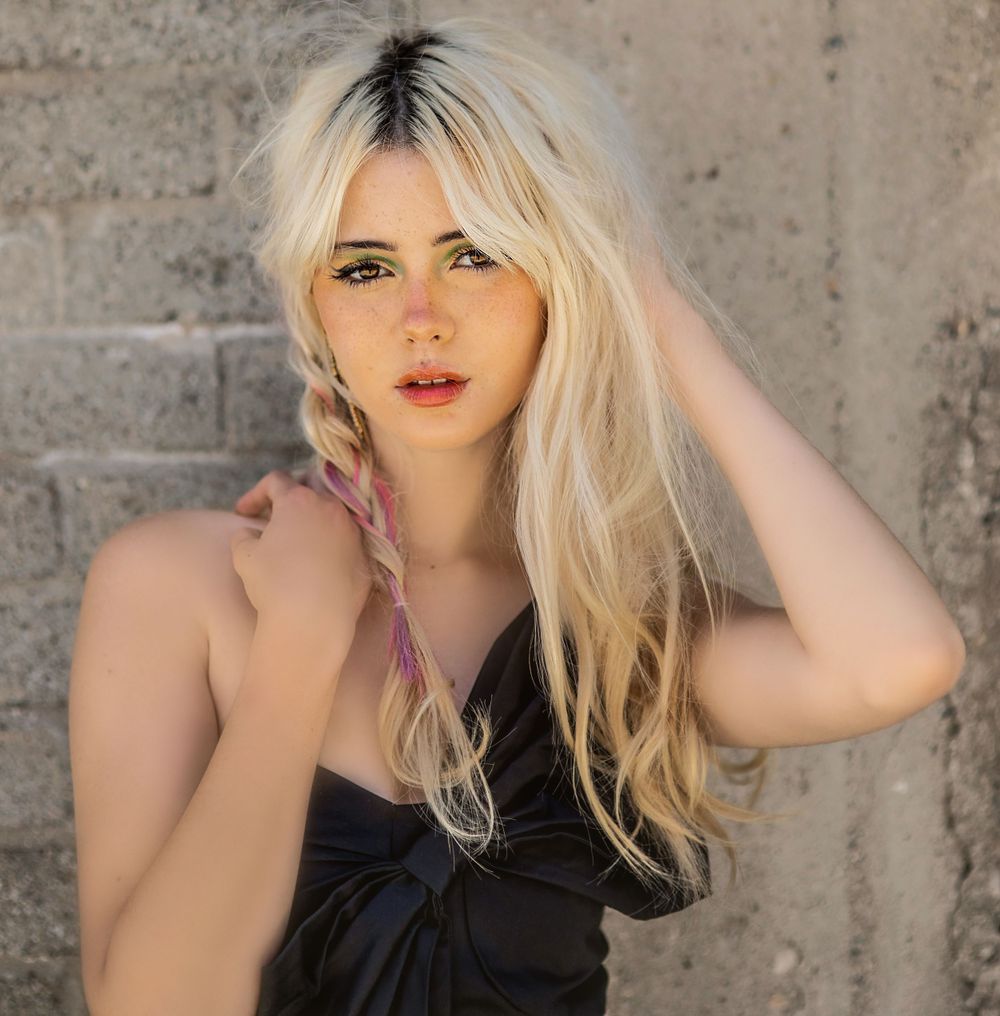 Portrait of a woman with platinum blonde hair and red lips against a concrete wall.
