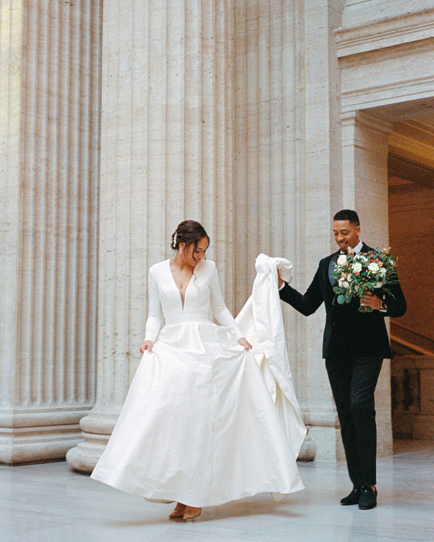 A playful wedding moment captured between classical stone columns.