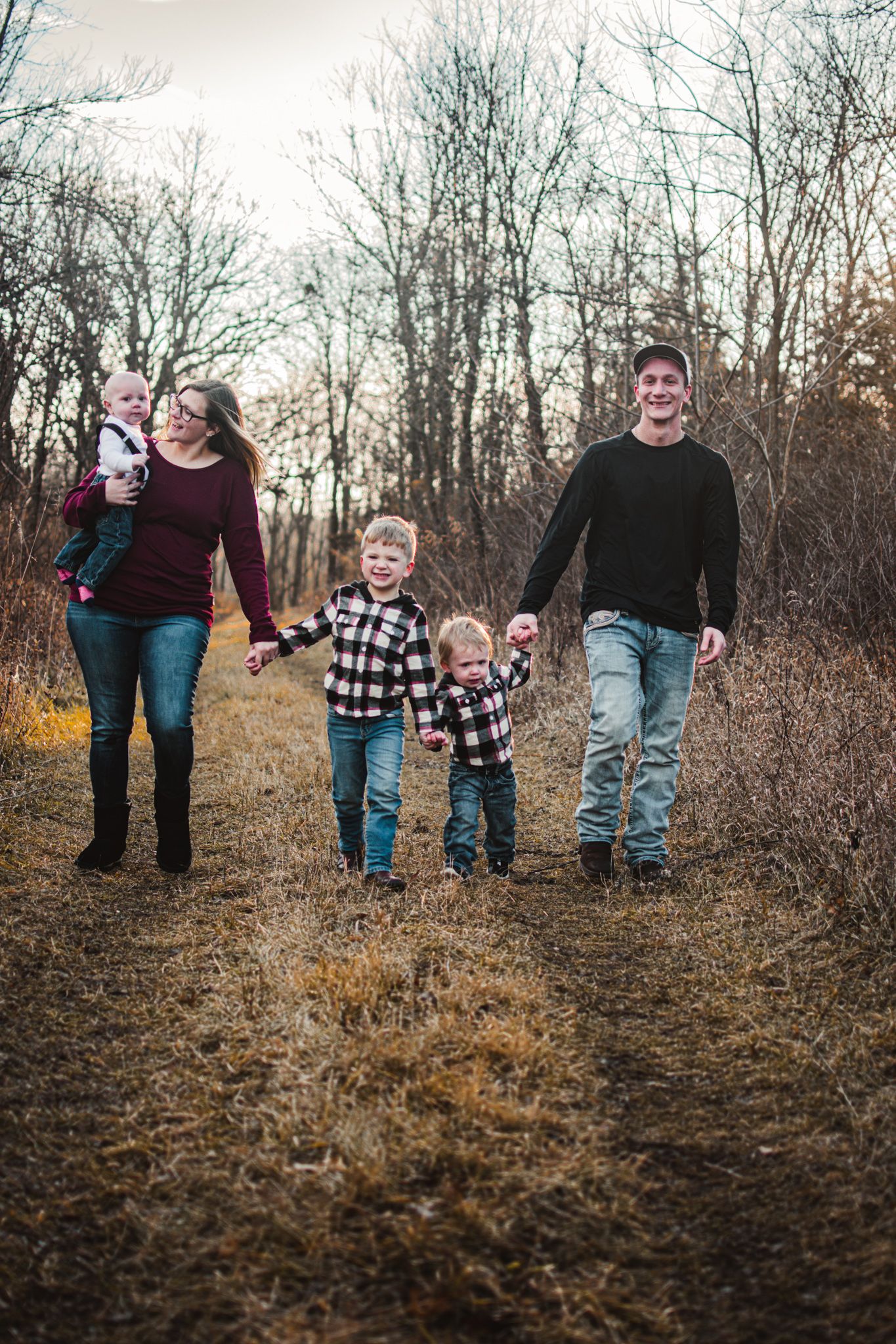 A family walks together on a nature trail during autumn surrounded by bare trees.