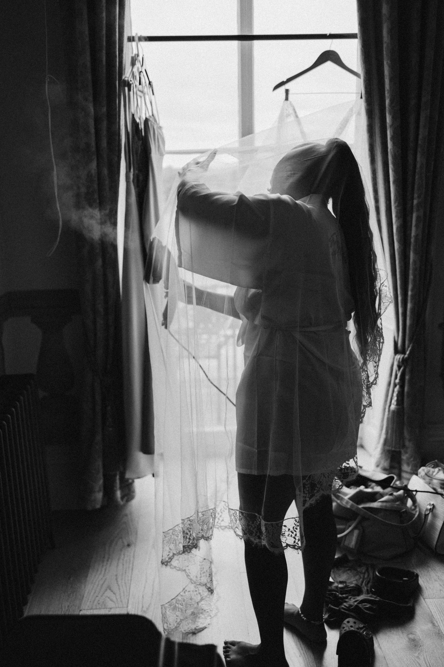 A silhouette of a person standing by a window with hanging clothes and natural light streaming in.