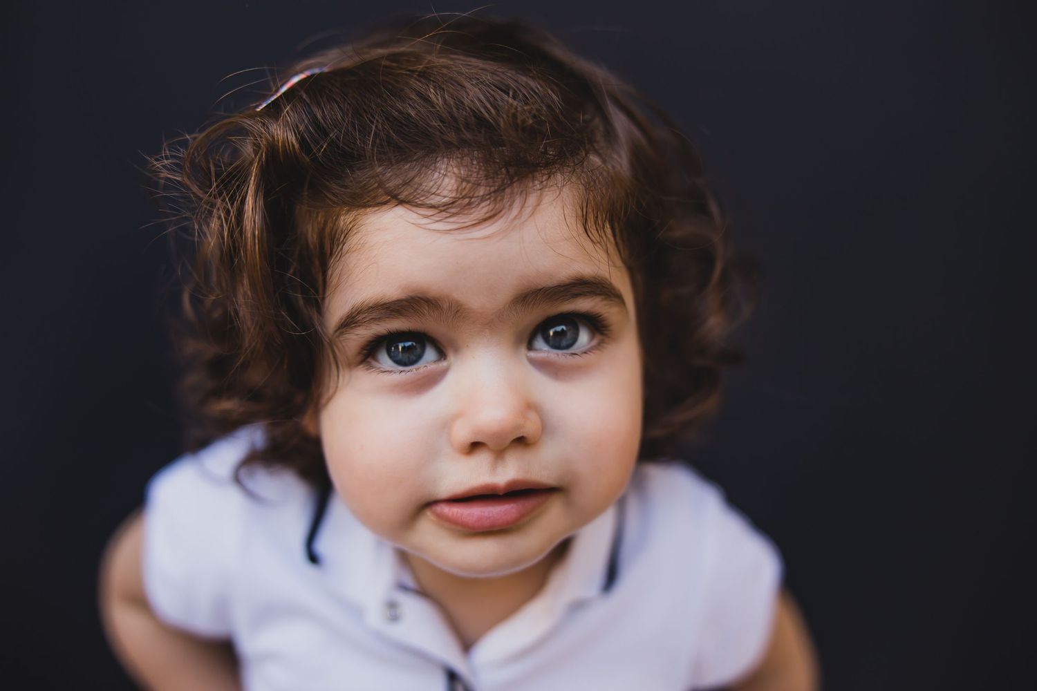 Close-up portrait of young child with curly hair and striking blue eyes looking at camera.